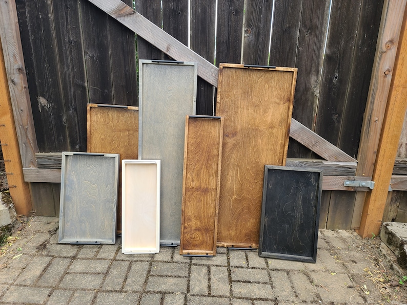 Puede incluir: Siete bandejas de madera de diferentes tama&ntilde;os y colores. Las bandejas est&aacute;n hechas de madera y tienen asas de metal negro. Las bandejas est&aacute;n dispuestas en una fila sobre una superficie de ladrillo.