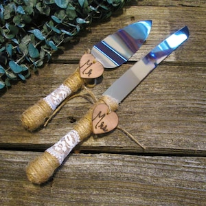 May include: A set of two cake cutting knives with wooden handles wrapped in twine and lace. The handles are decorated with wooden heart-shaped tags that say "Mr." and "Mrs."
