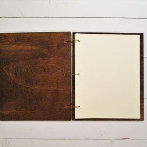 Puede incluir: Un cuaderno con cubierta de madera marr&oacute;n y p&aacute;ginas blancas en blanco. El cuaderno est&aacute; cerrado y tiene un cierre de cuerda.