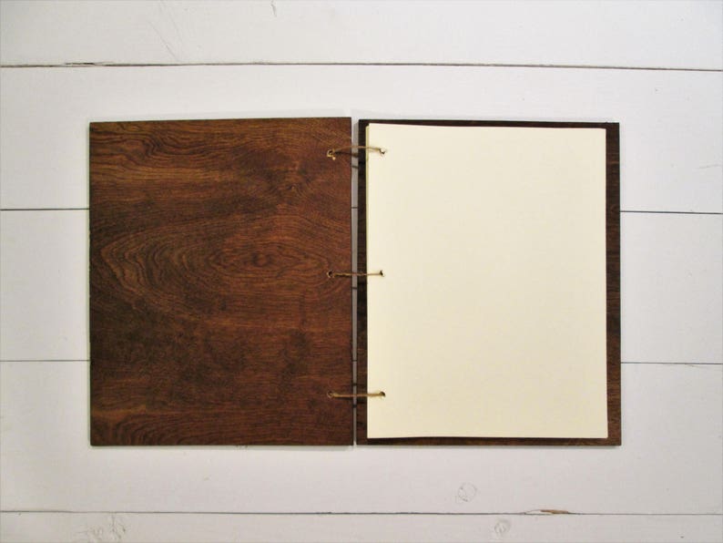 Puede incluir: Un cuaderno con cubierta de madera marr&oacute;n y p&aacute;ginas blancas en blanco. El cuaderno est&aacute; cerrado y tiene un cierre de cuerda.