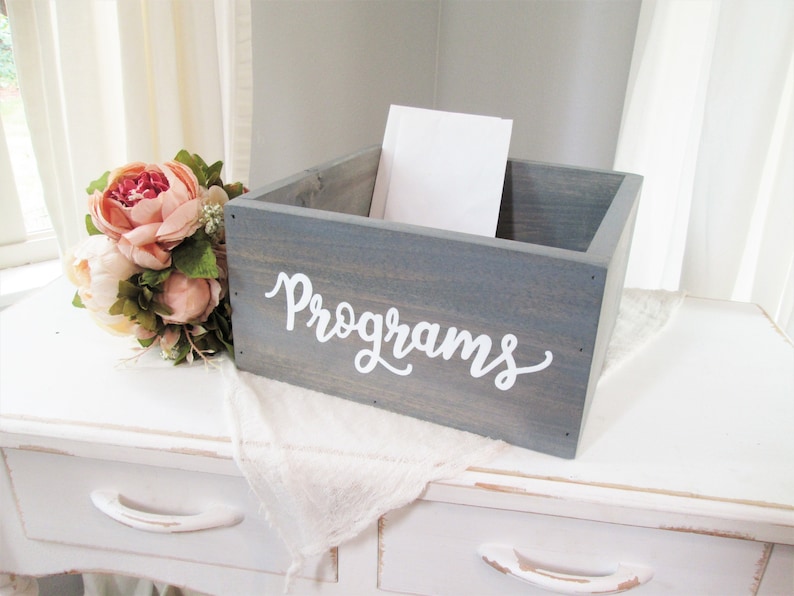May include: A gray wooden box with the word "Programs" written in white on the front. The box is sitting on a white table with a white cloth on top.