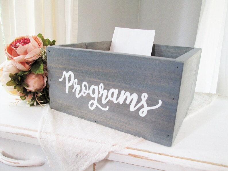 May include: A grey wooden box with the word "Programs" written in white cursive lettering. The box is sitting on a white surface.