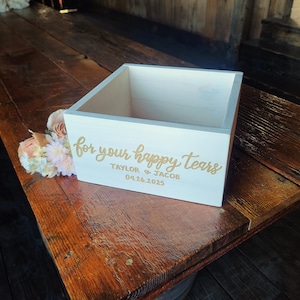 Pode incluir: Caixa de madeira branca com o texto "for your happy tears" em letras douradas. A caixa &eacute; personalizada com os nomes "Taylor & Jacob" e a data "04.26.2025".