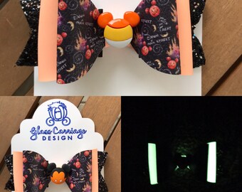 Puede incluir: Un lazo para el pelo de Halloween de color negro y naranja con una cabeza de Mickey Mouse que brilla en la oscuridad y un caramelo de maíz. El lazo tiene una tela de purpurina negra y naranja y un estampado de cabezas de Mickey Mouse, calabazas y las palabras "Trick or Treat" y "Down Main Street".