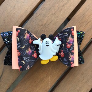 May include: A black and orange bow with a white ghost Mickey Mouse character in the center. The bow has a black and white print with the text "Down Main Street" and "Trick or Treat".