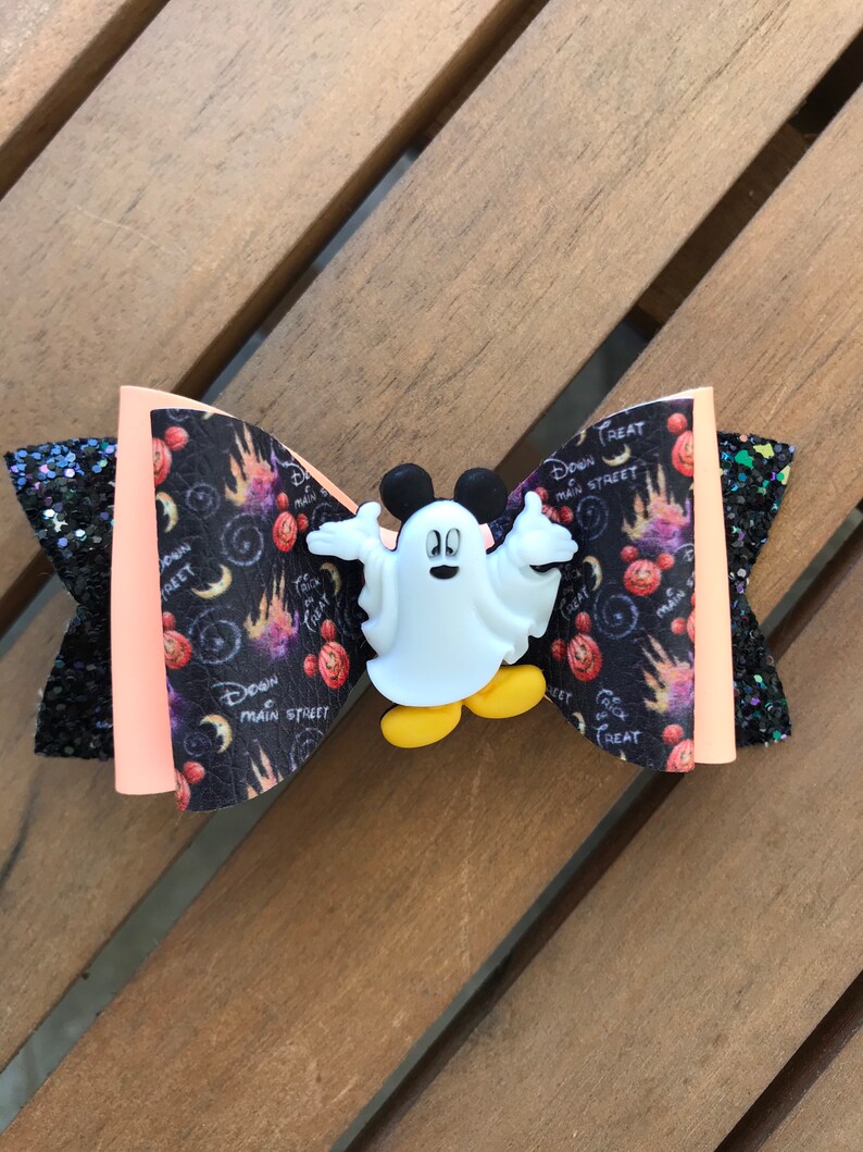May include: A black and orange bow with a white ghost Mickey Mouse character in the center. The bow has a black and white print with the text "Down Main Street" and "Trick or Treat".