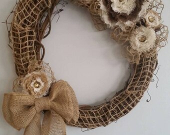 May include: A brown burlap wreath with a large burlap bow and several brown and white fabric flowers with gold accents.