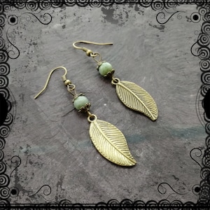 May include: A pair of gold leaf earrings with green stone accents. The earrings are made of metal and have a delicate, feminine design.