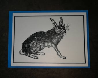 Może przedstawiać: Czarno-biała ilustracja królika siedzącego na białym tle. Królik jest zwrócony w lewo i ma długie uszy i puszysty ogon.