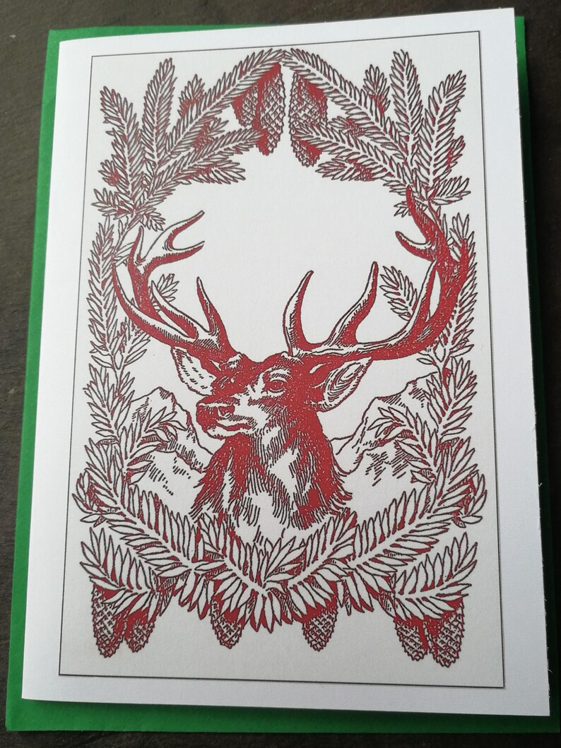 May include: A red and white illustration of a deer head with antlers framed by a wreath of pine branches and pine cones.