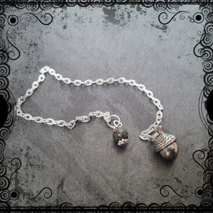 May include: A silver chain necklace with a green stone pendant and an acorn charm.