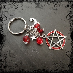 Op de afbeelding: Zilveren sleutelhanger met een rode pentagram-hanger, rode glazen kralen en zilveren sterren- en halve maan-charms.