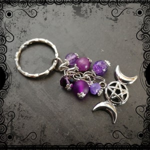 May include: A silver key chain with a triple moon and pentagram charm. The charm is adorned with purple and amethyst beads.