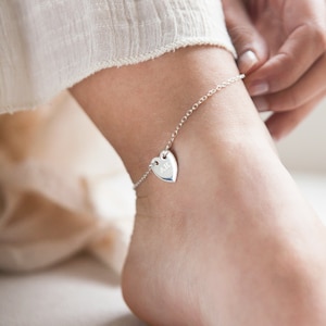 May include: A silver anklet with a heart-shaped charm engraved with the initials "AH".