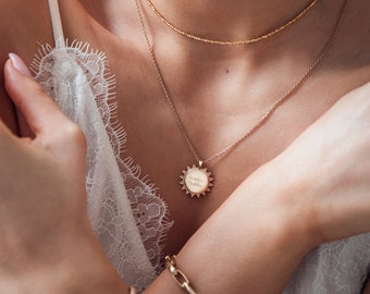 May include: A gold necklace with a delicate chain and a round pendant that says "Sweetest Rebellion".