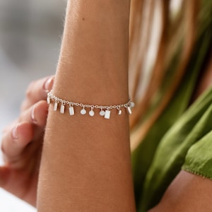 May include: A silver charm bracelet with a delicate chain and various small silver charms, including squares, rectangles, and circles.