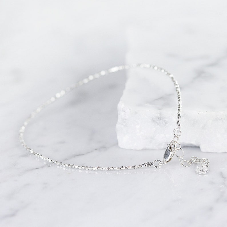 May include: A delicate silver chain anklet with a lobster clasp closure. The chain is made of small, round beads.
