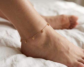 May include: A delicate gold-toned chain anklet featuring small, evenly spaced spherical charms dangling along the length of the chain. The anklet is worn around the ankle, showcasing a simple link design with a polished metallic finish throughout.