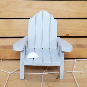 May include: A miniature light blue wooden adirondack chair with a white seashell on the seat.