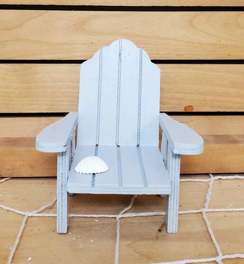 May include: A miniature light blue wooden adirondack chair with a white seashell on the seat.