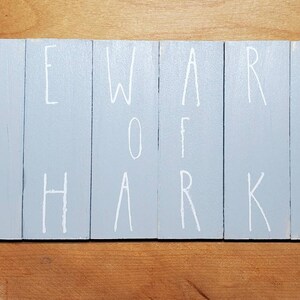 May include: A light blue wooden sign with the words "BEWARE OF SHARKS" written in white paint.