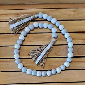May include: A garland of light blue and white wooden beads with two brown and white tassels.