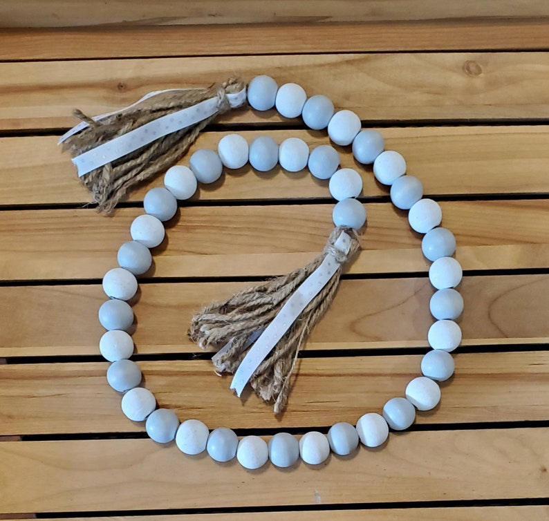 May include: A garland of light blue and white wooden beads with two brown and white tassels.