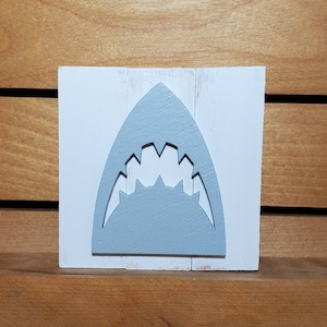 May include: A white wooden sign with a grey shark tooth cutout. The sign is distressed and has a rustic look.