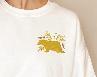 May include: White sweatshirt with a yellow bear silhouette and the words "loyal" and "kind" in brown text.