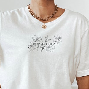 May include: White oversized t-shirt with a floral design and the text "[inhales deeply]" printed on the front.