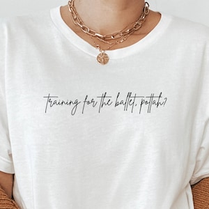 May include: White t-shirt with the text "Training for the ballet, pfft ah?" printed in black.