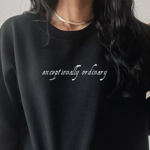 Puede incluir: Sudadera negra con el texto "excepcionalmente ordinario" en letras blancas.