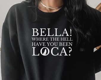 Puede incluir: Sudadera negra con texto blanco: "BELLA! WHERE THE HELL HAVE YOU BEEN LOCA?". El texto está centrado. La sudadera es de cuello redondo.
