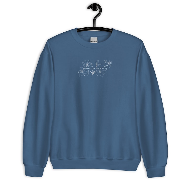 May include: A blue sweatshirt with a white floral design and the text "[INHALES DEEPLY]" printed on the front.