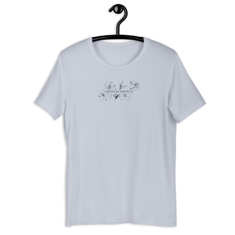 May include: A light blue t-shirt with a floral design and the text "[inhales deeply]" printed on the front.