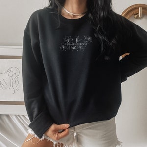 May include: Black sweatshirt with a white floral design and the text "[INHALES DEEPLY]" printed on the front.