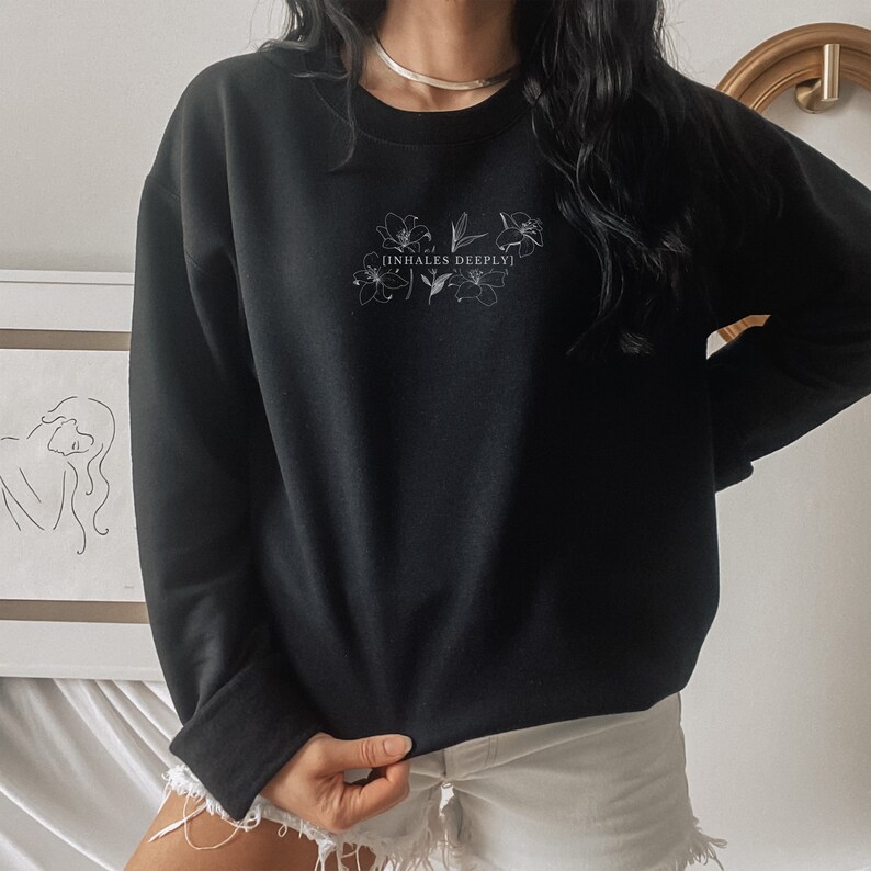 May include: Black sweatshirt with a white floral design and the text "[INHALES DEEPLY]" printed on the front.