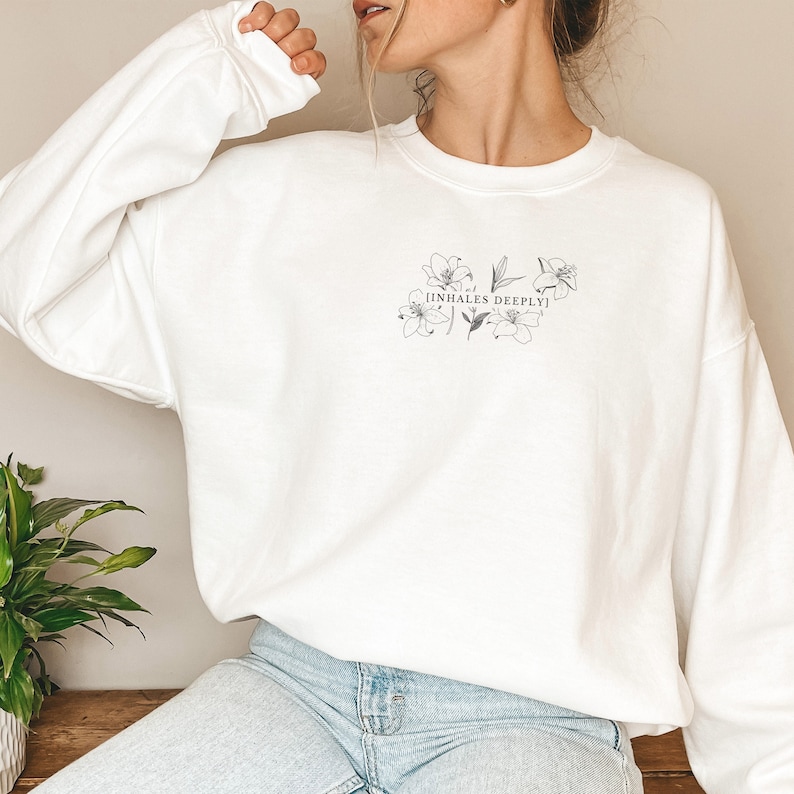 May include: White sweatshirt with a floral design and the text "INHALES DEEPLY" printed on the front.