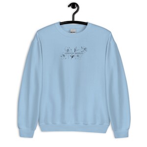 May include: Light blue sweatshirt with a black floral design and the text "[INHALES DEEPLY]" printed on the front.