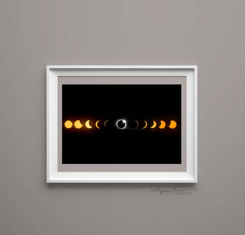 May include: A black and white photograph of a solar eclipse. The image shows the sun being covered by the moon, with a ring of light around the moon. The image is framed in a white frame.