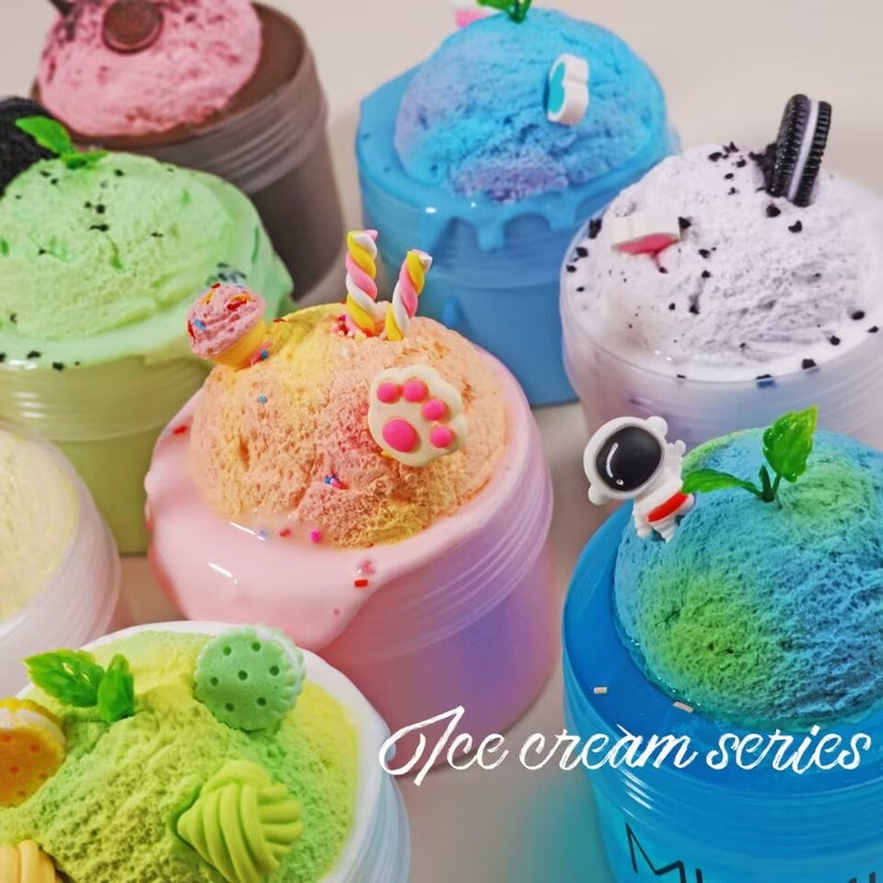 May include: A collection of colorful, decorative slimes resembling ice cream. Each slime is in a clear plastic container and topped with various embellishments like sprinkles, cookies, and miniature figurines. The text "Ice cream series" is visible.