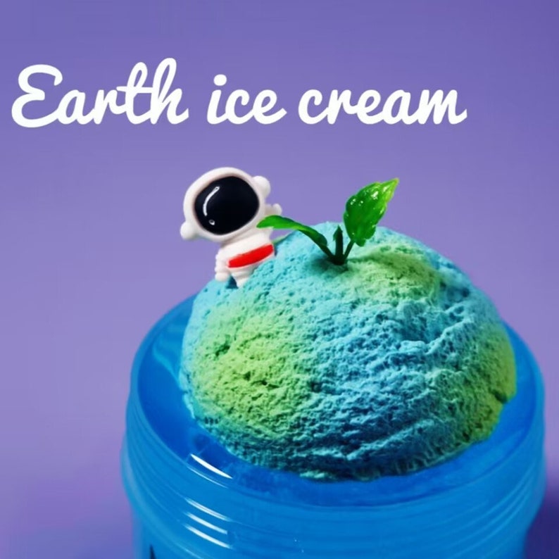 May include: A scoop of blue and green ice cream resembling Earth, with a tiny astronaut figurine and a green leaf. The ice cream is in a blue cup, and the text "Earth ice cream" is written in white.