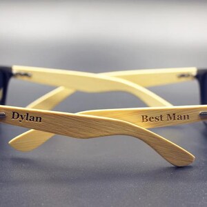 May include: A pair of black sunglasses with wooden arms. The arms are engraved with the words "Dylan" and "Best Man".