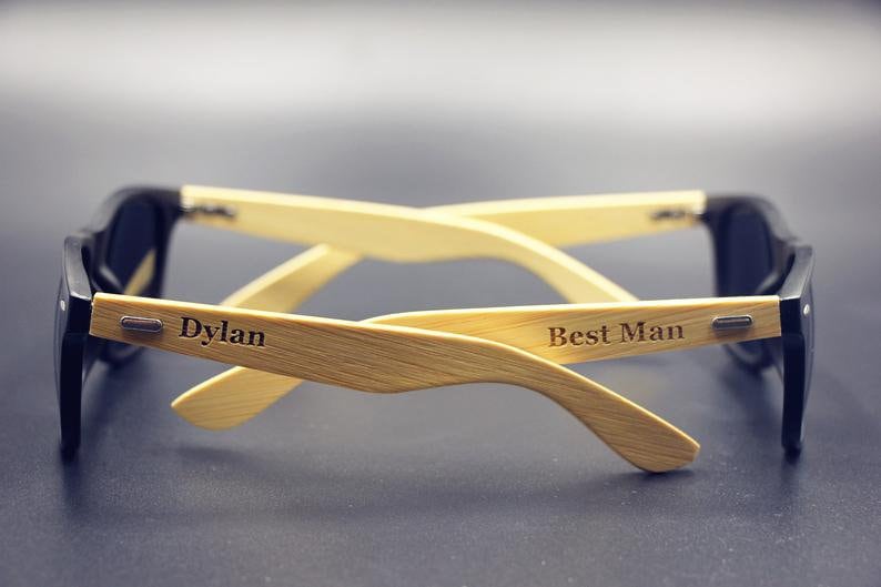 May include: A pair of black sunglasses with wooden arms. The arms are engraved with the words "Dylan" and "Best Man".