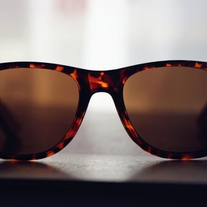 May include: Tortoiseshell sunglasses with brown lenses. The sunglasses are sitting on a dark surface.