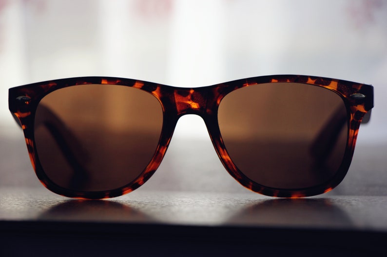 May include: Tortoiseshell sunglasses with brown lenses. The sunglasses are sitting on a dark surface.