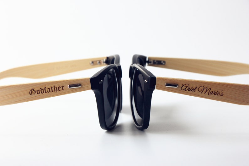 May include: Two pairs of black sunglasses with bamboo frames. One frame is engraved with "Godfather" and the other with "Ariel Marie's".