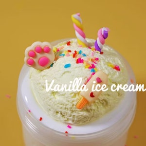 May include: A container of vanilla ice cream with colorful sprinkles, a paw-shaped decoration, and a popsicle. The ice cream is topped with two twisted, colorful candies. The text "Vanilla ice cream" is written on the ice cream.