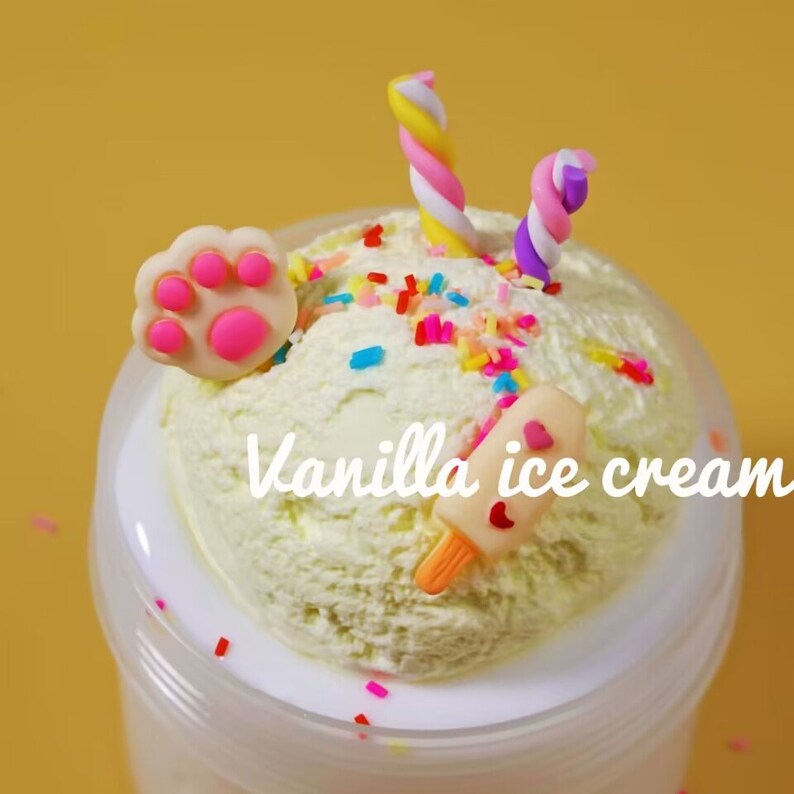 May include: A container of vanilla ice cream with colorful sprinkles, a paw-shaped decoration, and a popsicle. The ice cream is topped with two twisted, colorful candies. The text "Vanilla ice cream" is written on the ice cream.