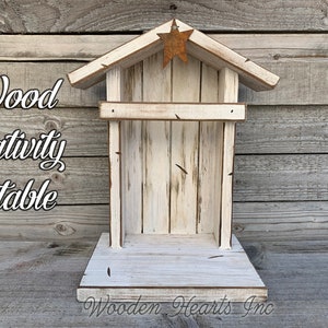 May include: White wooden nativity stable with a rustic star on the roof. The stable is made of weathered wood and has a distressed white paint finish. The text "Wooden Hearts Inc." is printed on the base of the stable.
